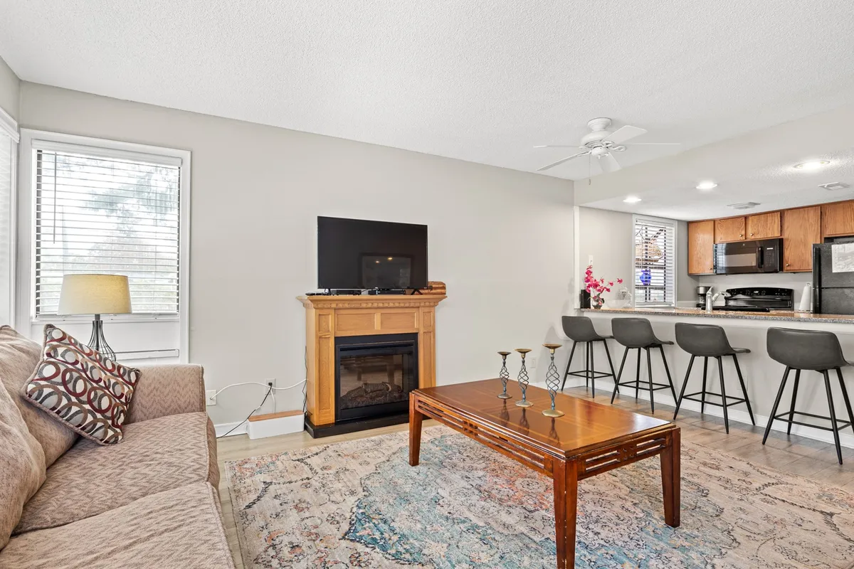 An inviting open-concept space featuring a sofa and coffee table near a fireplace, seamlessly connected to a kitchen bar. The layout naturally promotes interaction, making it ideal for entertaining and shared moments.
