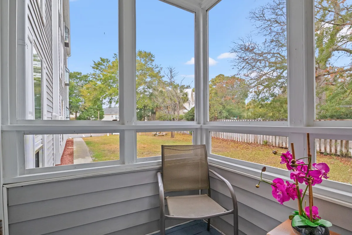 A cozy screened porch with a comfortable chair and a flower arrangement overlooks a peaceful garden view. The scene suggests a seamless transition from indoor dining to enjoying meals or drinks outdoors in a tranquil setting.
