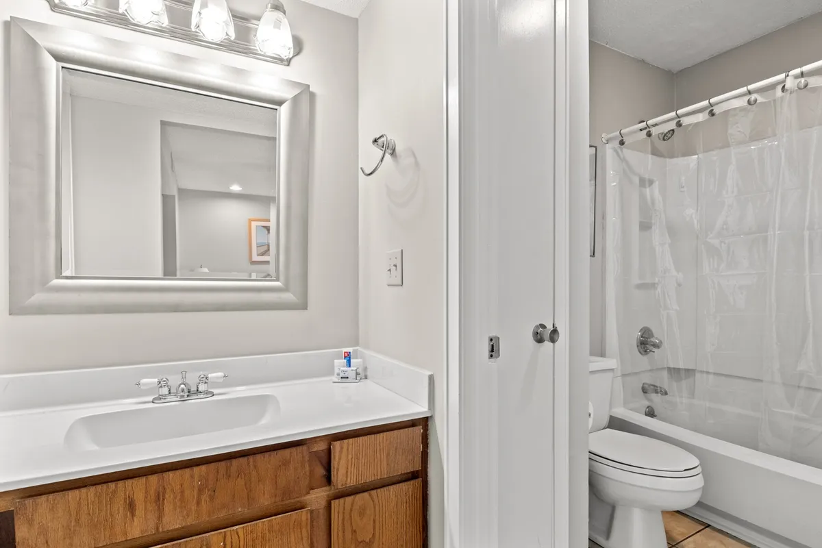A gleaming bathroom features a sink with vanity, a well-lit mirror, and a shower with a curtain. The space is fresh and inviting, designed for relaxation and efficient routines.