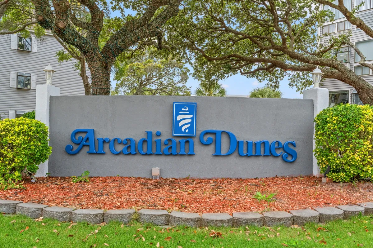 A welcoming exterior shot of the Arcadian Dunes sign surrounded by lush landscaping and greenery. The setting is tranquil, emphasizing the sense of community and the resort’s inviting atmosphere.