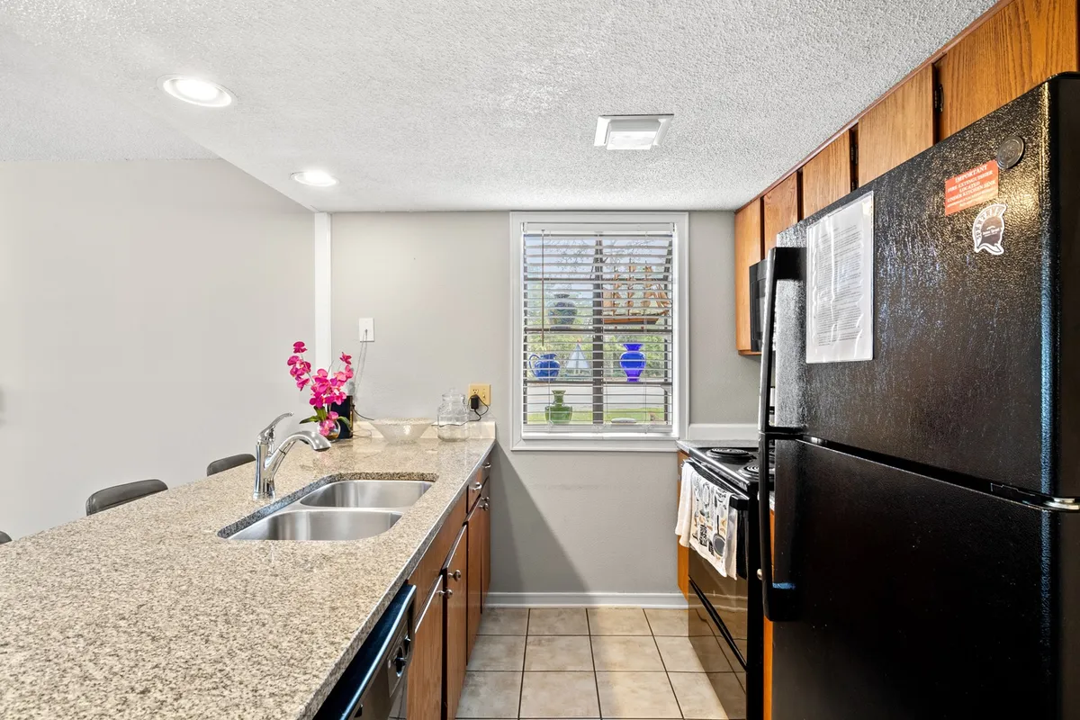 A modern kitchen with a granite countertop, black refrigerator, window showcasing a floral view, and a sink. The setup is bright and inviting, perfect for meal prep, coffee chats, and creating vacation memories.