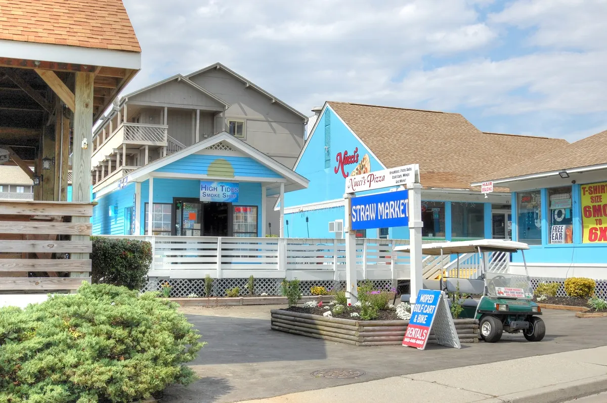 The image captures a lively street lined with colorful buildings and shops, including visible store signs and a golf cart parked outside. The area feels vibrant, welcoming, and ideal for leisurely exploration, dining, and shopping.